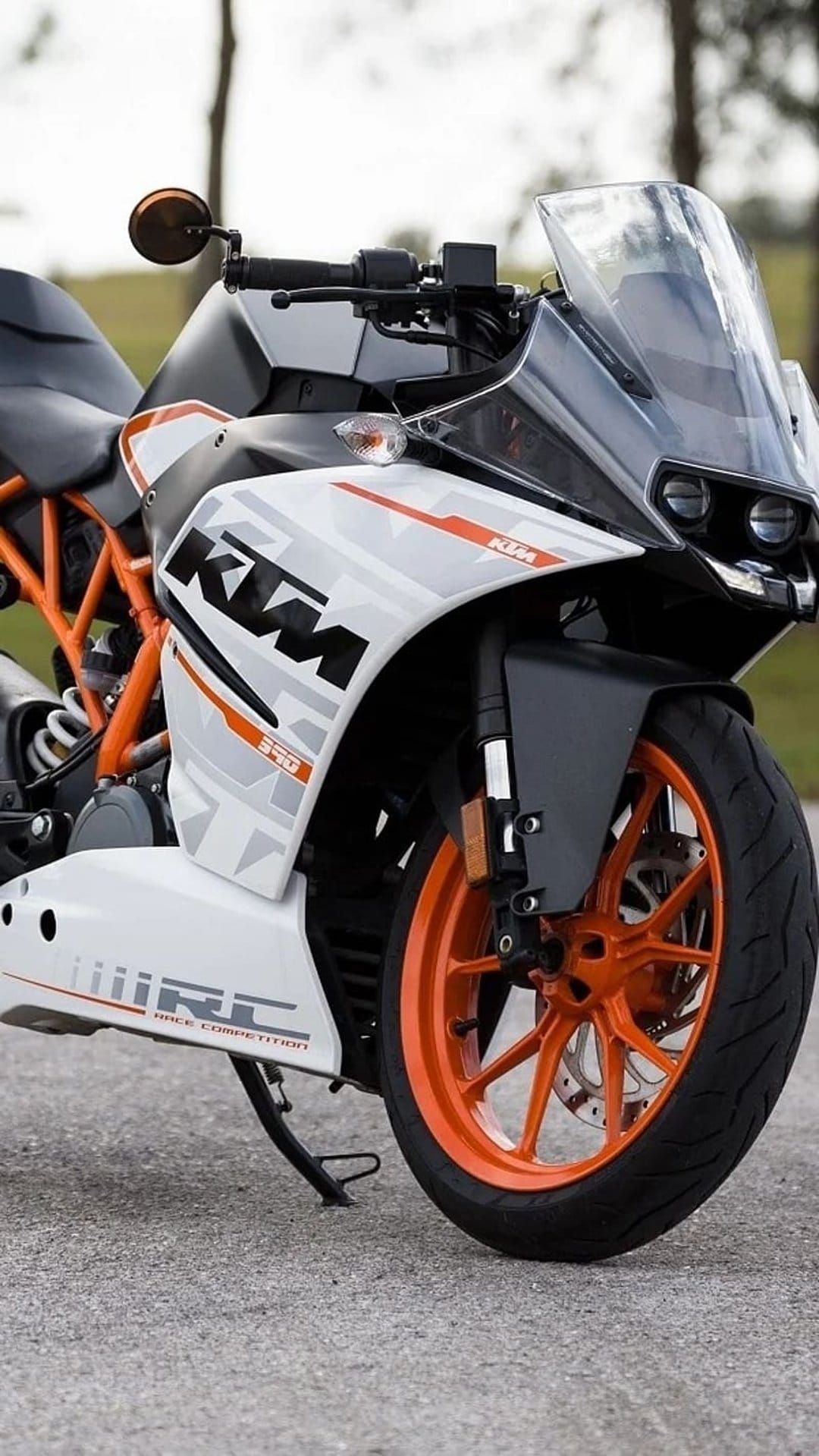 KTM RC 390 motorcycle features a white fairing, orange wheels, and a tinted windscreen in a close-up front view.