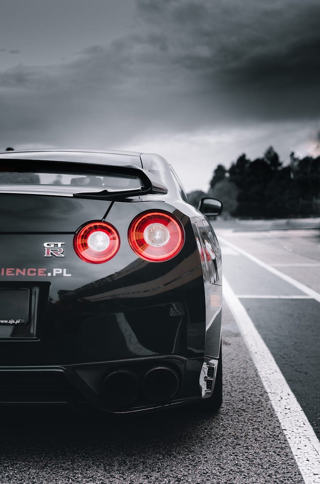 Black Nissan GT-R rear view with glowing red circular taillights on a road under a dark overcast sky.