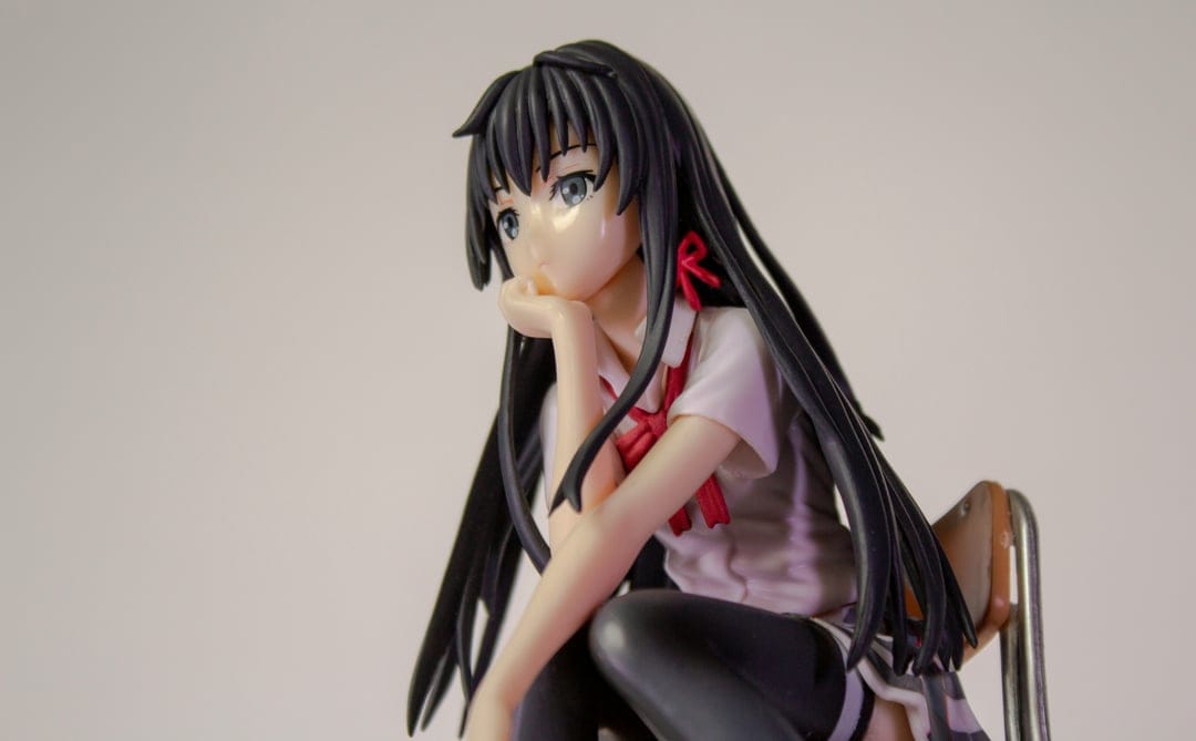 Anime girl figurine in a school uniform sits with her hand on her chin, featuring black hair and a red ribbon.