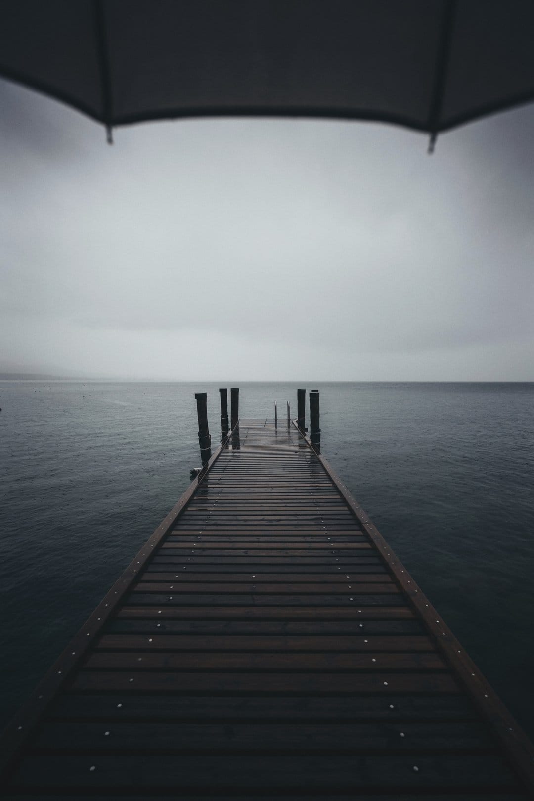 Weathered wooden pier leading into a vast misty lake under a heavy overcast sky with gray water and thick fog.
