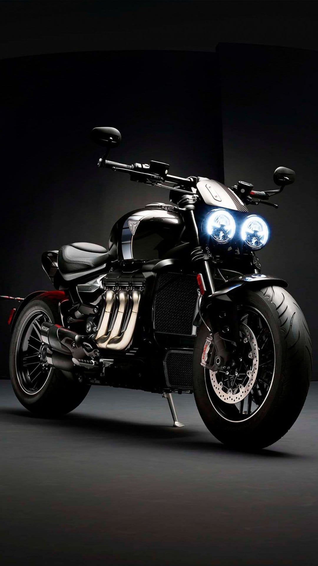 Triumph Rocket 3 motorcycle with glowing dual headlights, chrome exhaust pipes, and a muscular engine design.