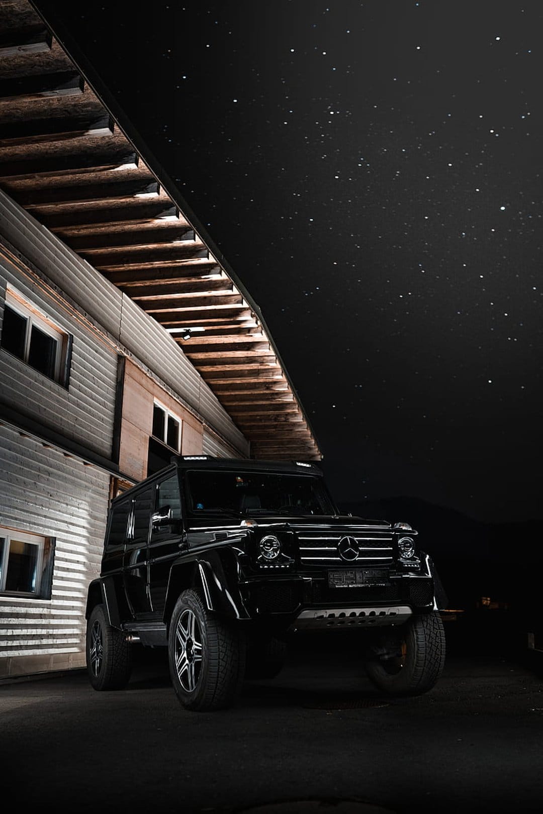 Black Mercedes G-Wagon parked beside a rustic building under a clear night sky filled with bright constellations.