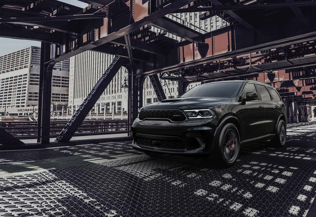 Black Dodge Durango SRT parked on a metal bridge deck framed by steel beams with a city skyline background.