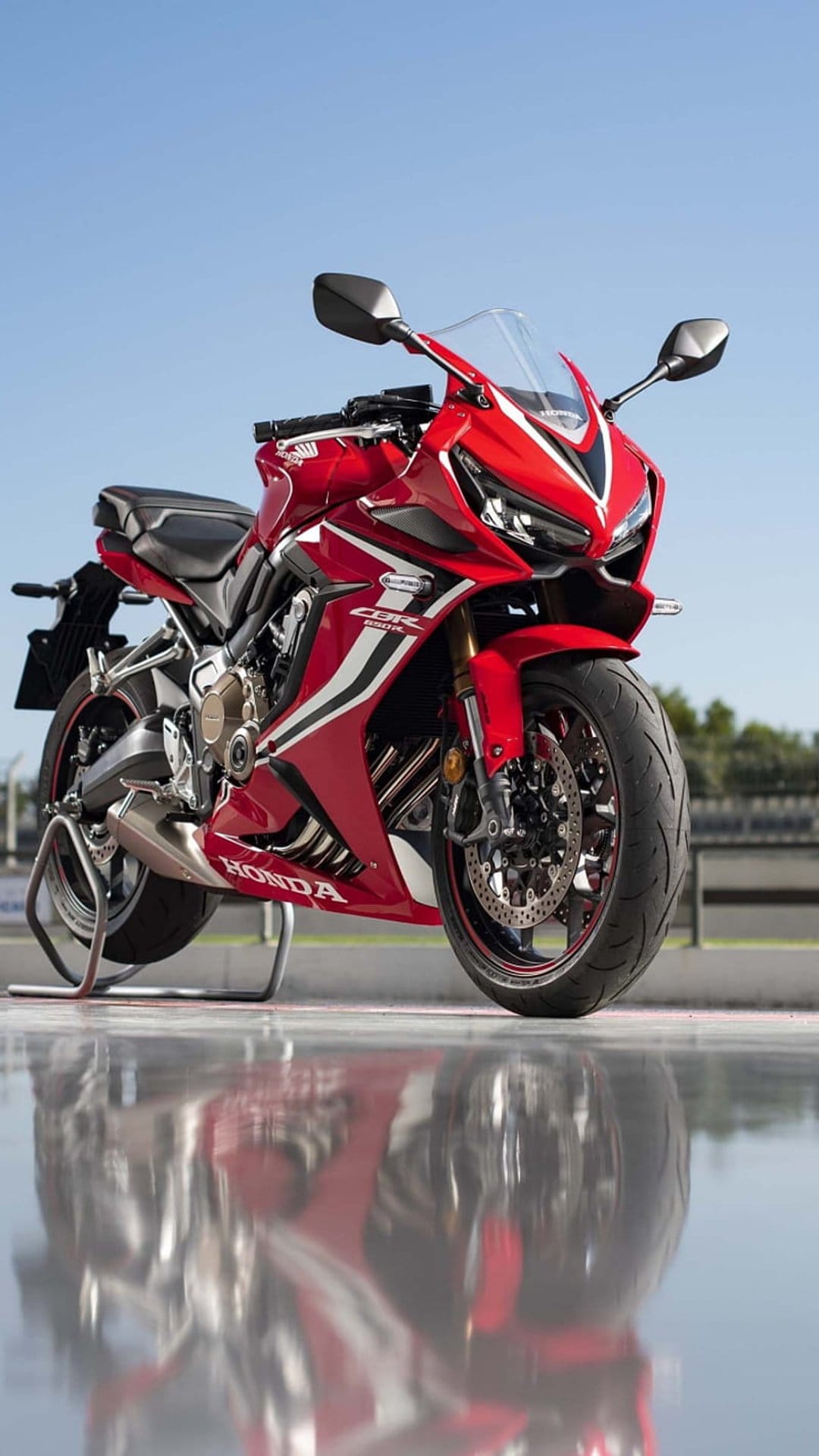 Red Honda CBR motorcycle reflecting on a wet racing track surface under a clear blue sky during the daytime.