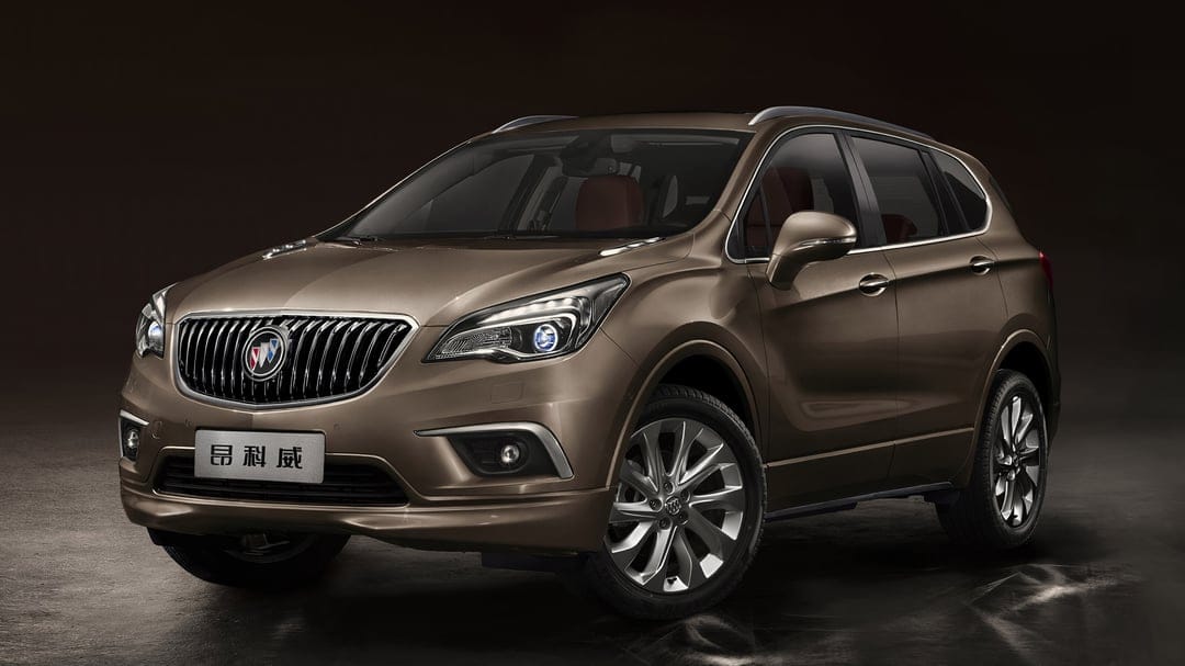 Metallic brown Buick Envision SUV with a chrome grille and alloy wheels in a dark studio environment.