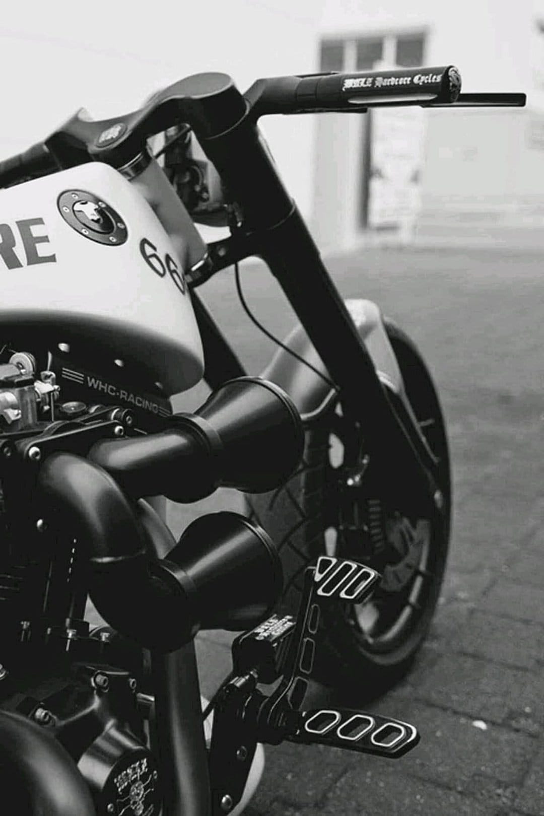 Custom Harley motorcycle handlebars and exhaust pipes with the number 66 on the tank in black and white.