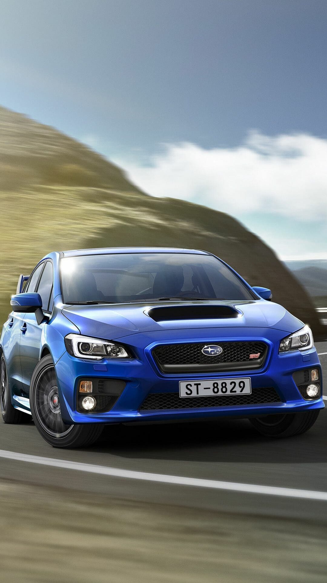 Blue Subaru WRX STI sports car driving fast on a scenic mountain road with motion blur and bright daylight.