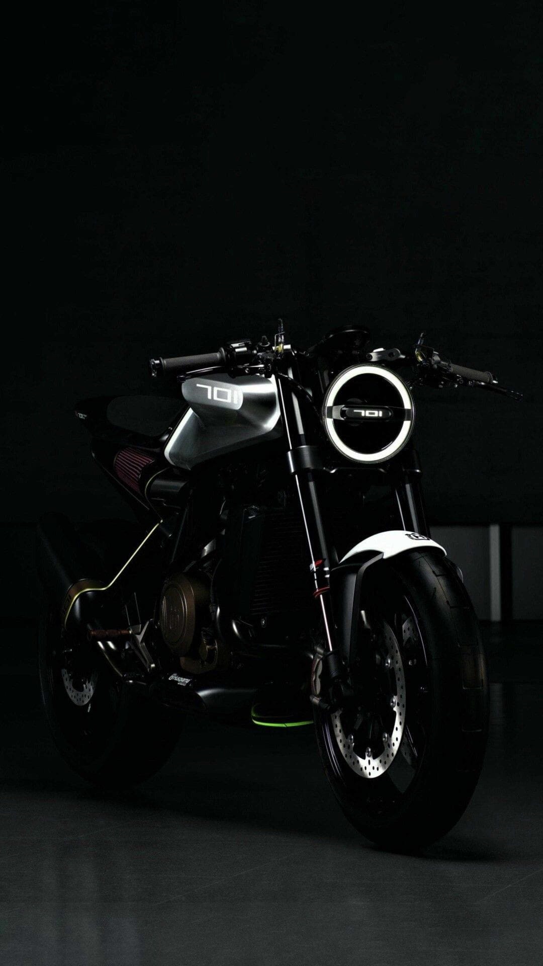 Black motorcycle with a circular 701 LED headlight glows against a dark background in a vertical studio shot.