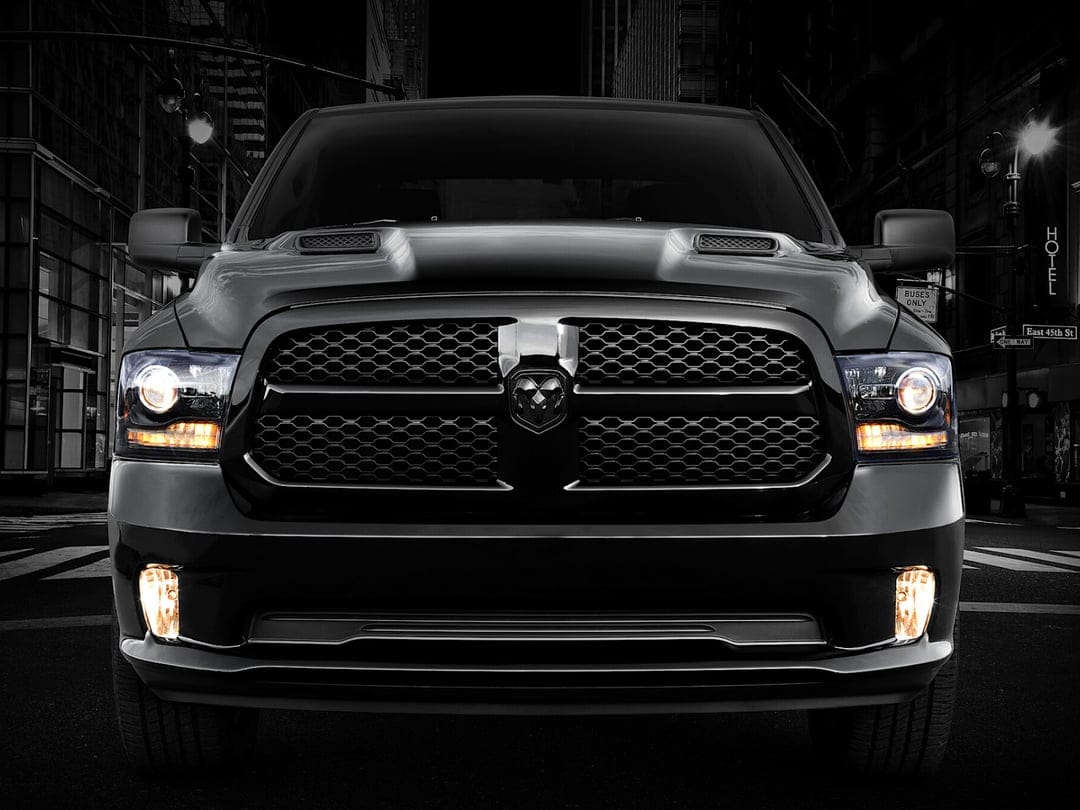 Front view of a black Ram truck with glowing amber headlights parked on a dark city street at night.