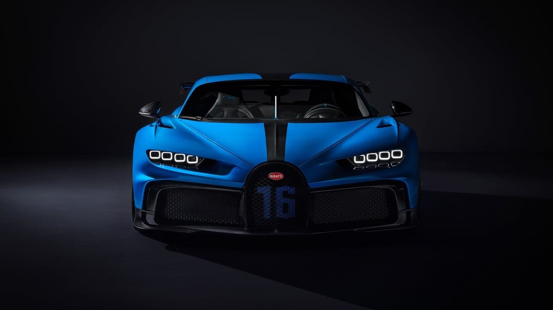 Blue Bugatti Chiron Pur Sport front view with glowing quad headlights and carbon fiber accents in a dark studio.