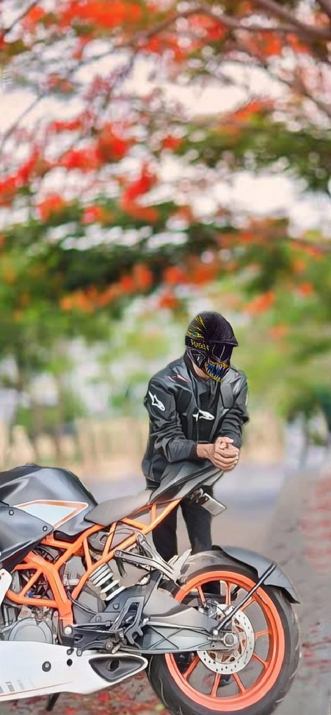Man in a black motorcycle helmet and jacket leans on a KTM bike with orange wheels amid blurry green trees.