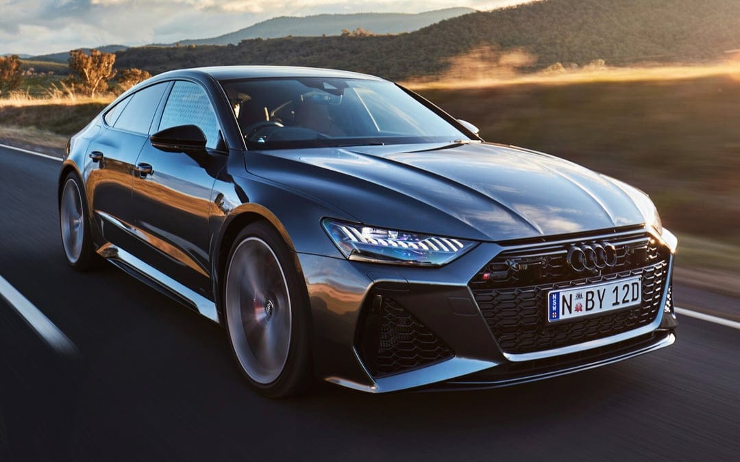 Audi RS7 Sportback driving on a scenic road during golden hour with blurred background and glowing headlights.