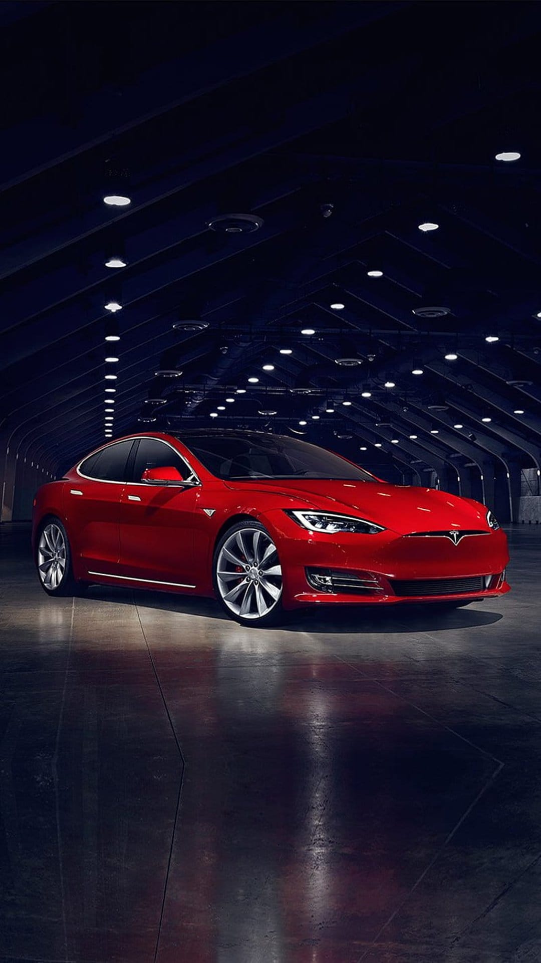 Red Tesla Model S sedan parked in a dark modern garage with overhead lighting and reflective concrete floors.