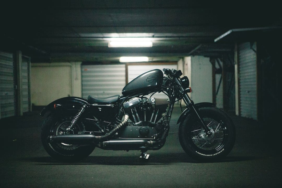Black Harley Davidson Sportster motorcycle in a dark garage with overhead lighting and metallic roll-up doors.