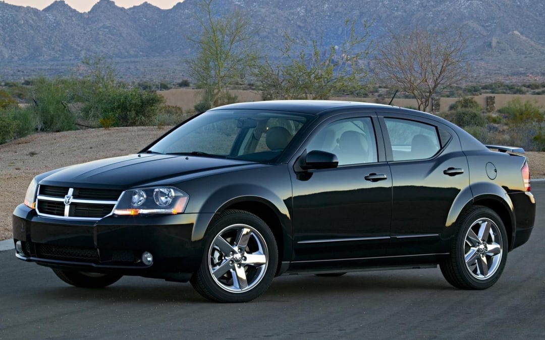 Black Dodge Avenger sedan with chrome wheels parked in a desert landscape with mountains in the background.
