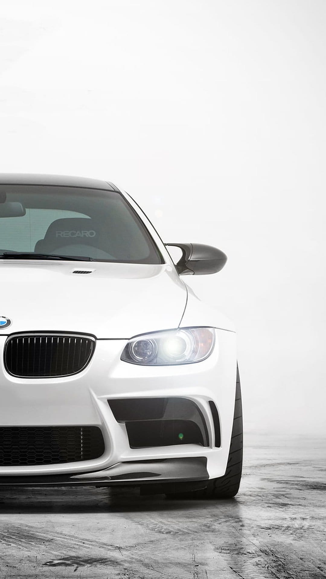 White BMW M3 coupe with LED headlights, carbon fiber splitter, and Recaro racing seats in a bright studio space.