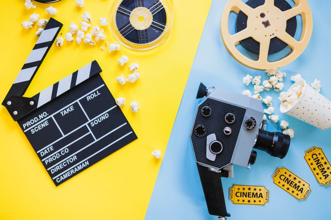 Vintage film camera, clapperboard, and popcorn are arranged on a vibrant yellow and blue split-tone background.