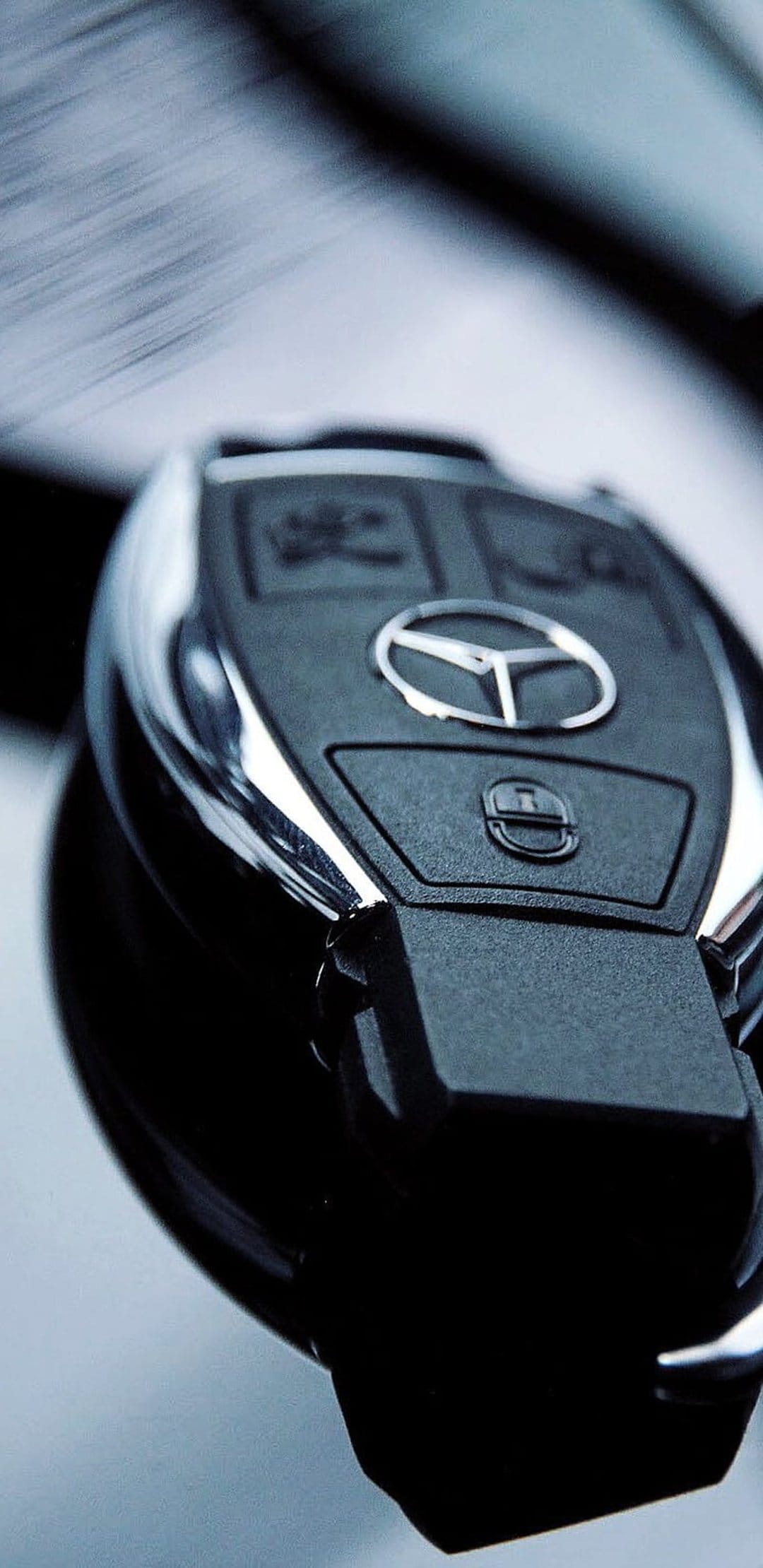 Mercedes-Benz car key fob featuring a silver logo, textured black surface, and chrome buttons on a blurred backdrop.