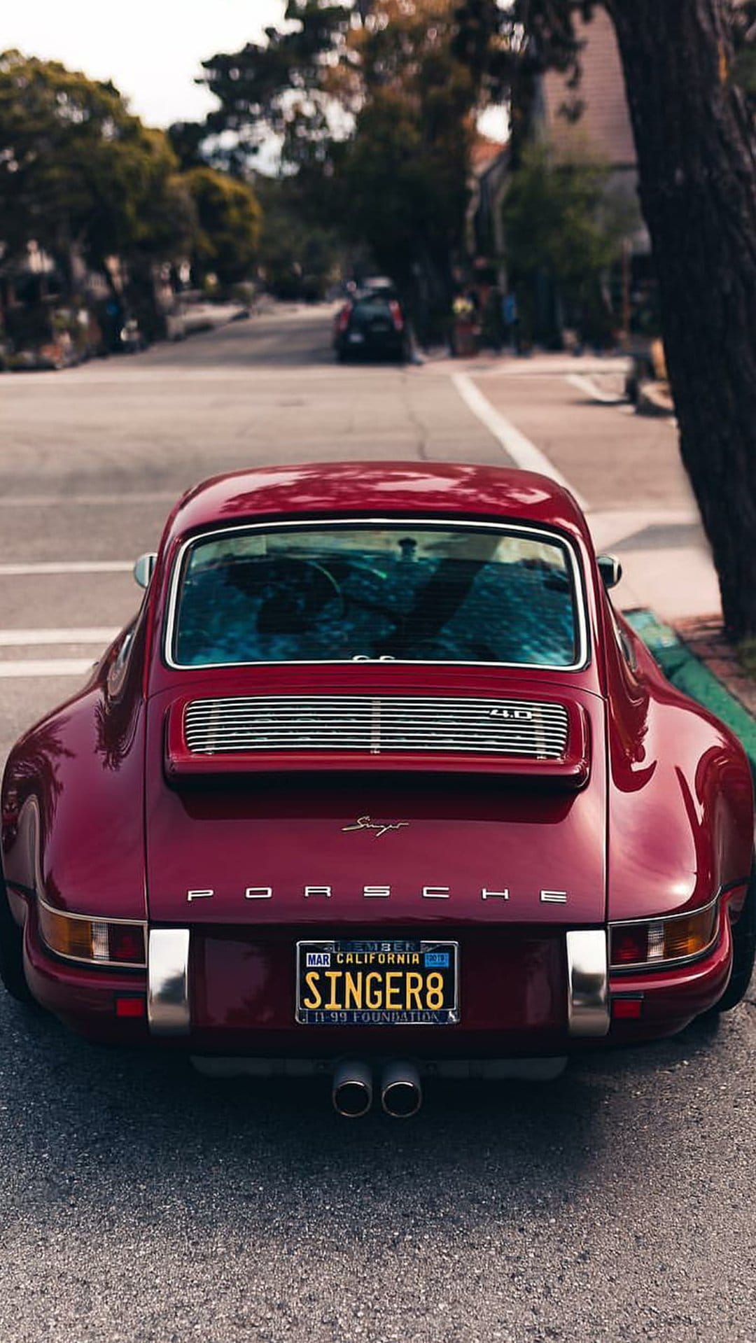 Red Porsche Singer 911 rear view with custom taillights and a California plate on a sunlit residential street.