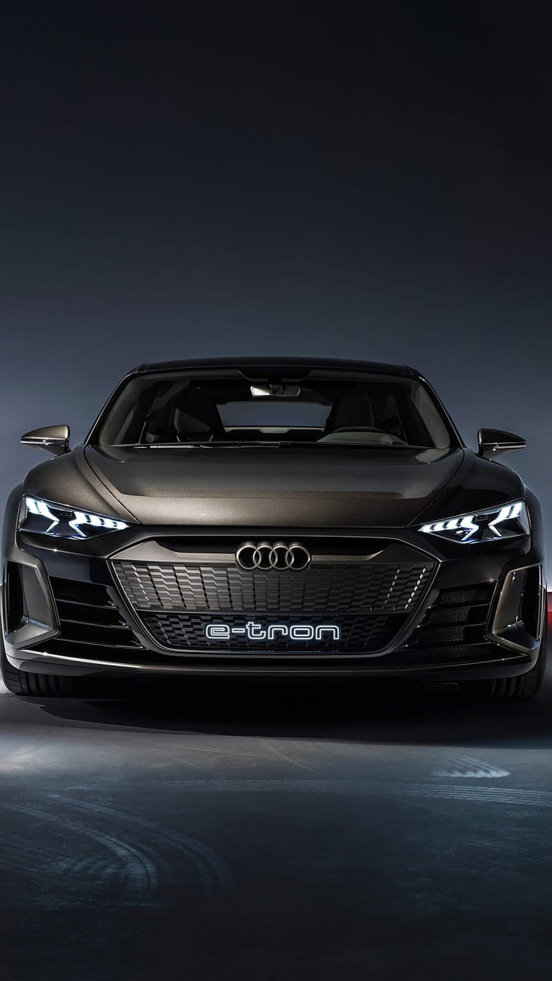 Audi e-tron concept car front fascia with illuminated LED headlights and silver rings on a dark background.