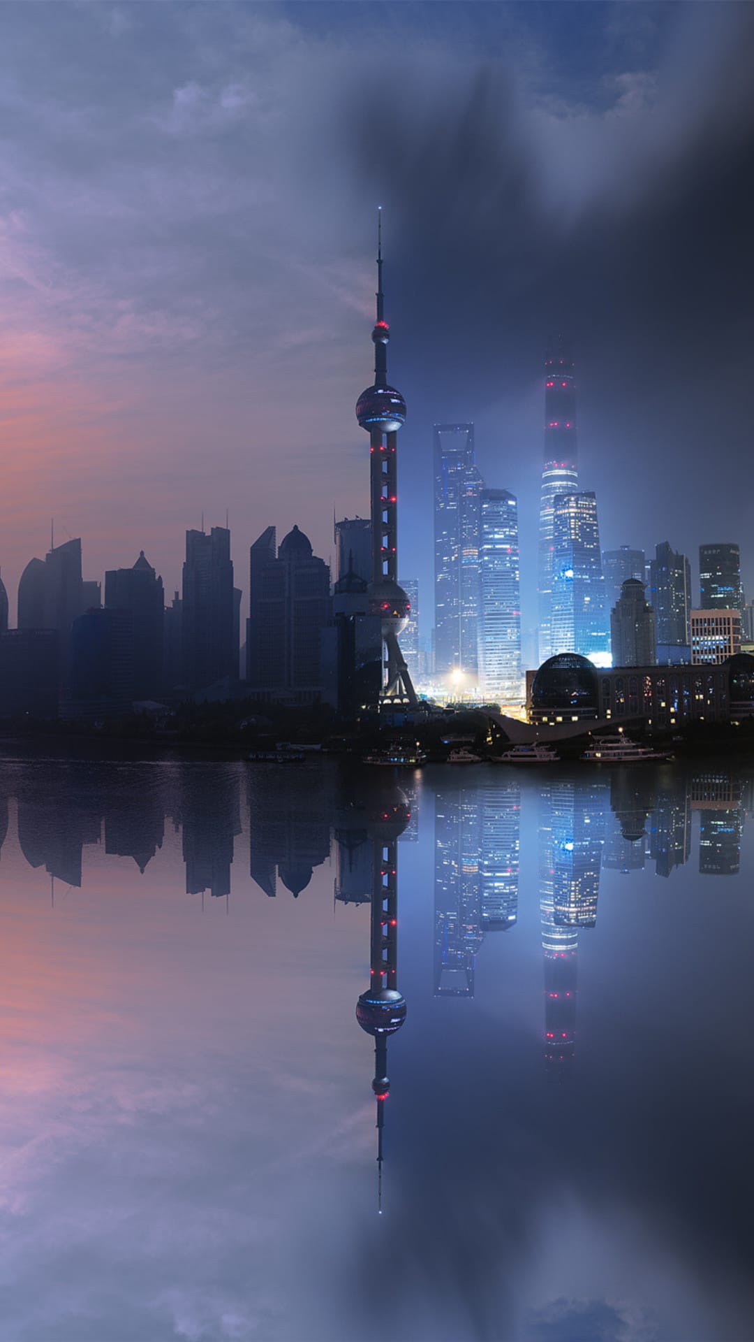 Illuminated skyscrapers with spherical pods reflect in calm harbor water under a violet midnight sky.