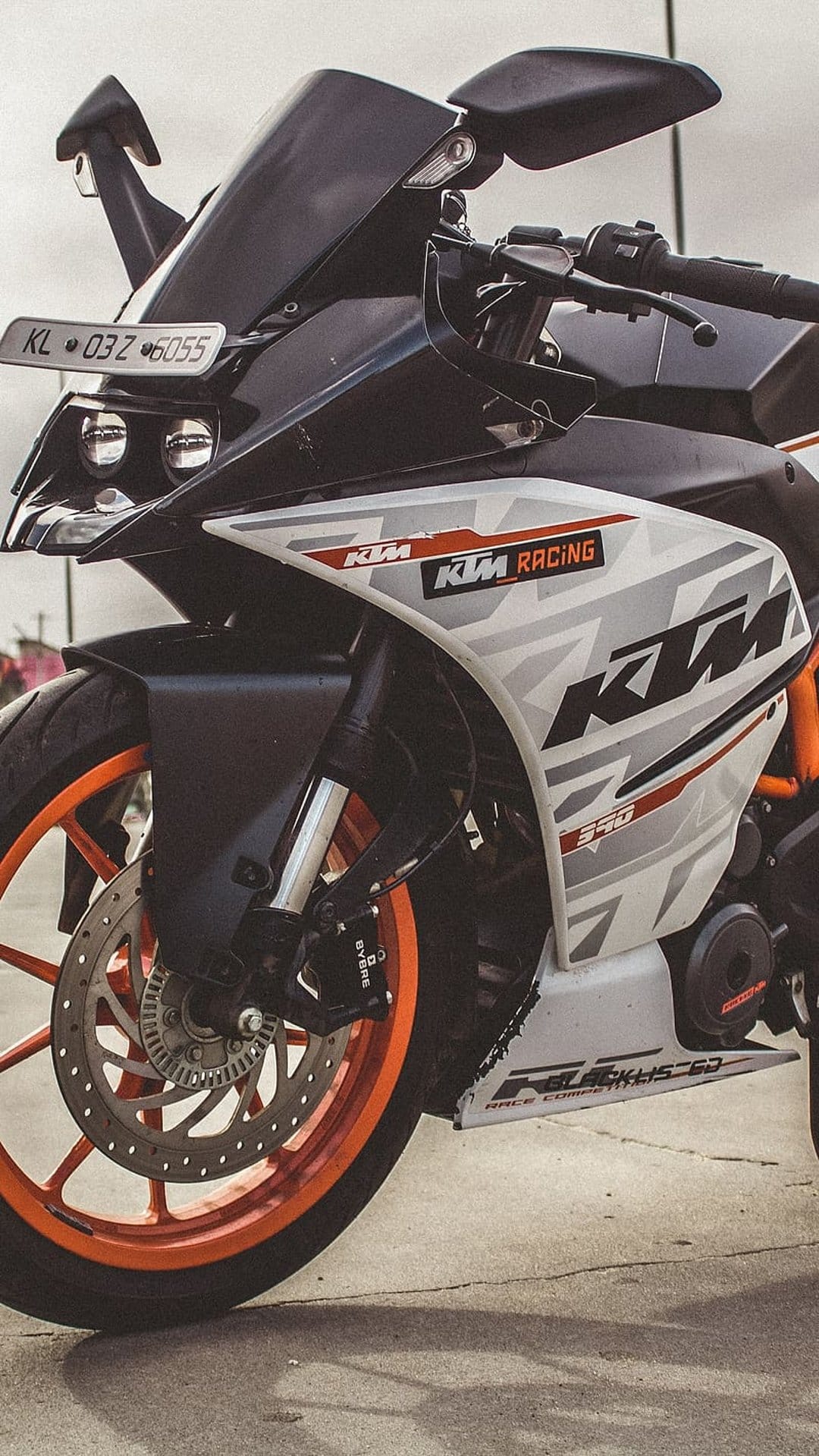 KTM RC 390 motorcycle front with dual headlights, racing decals, and bright orange wheels on a vertical display.