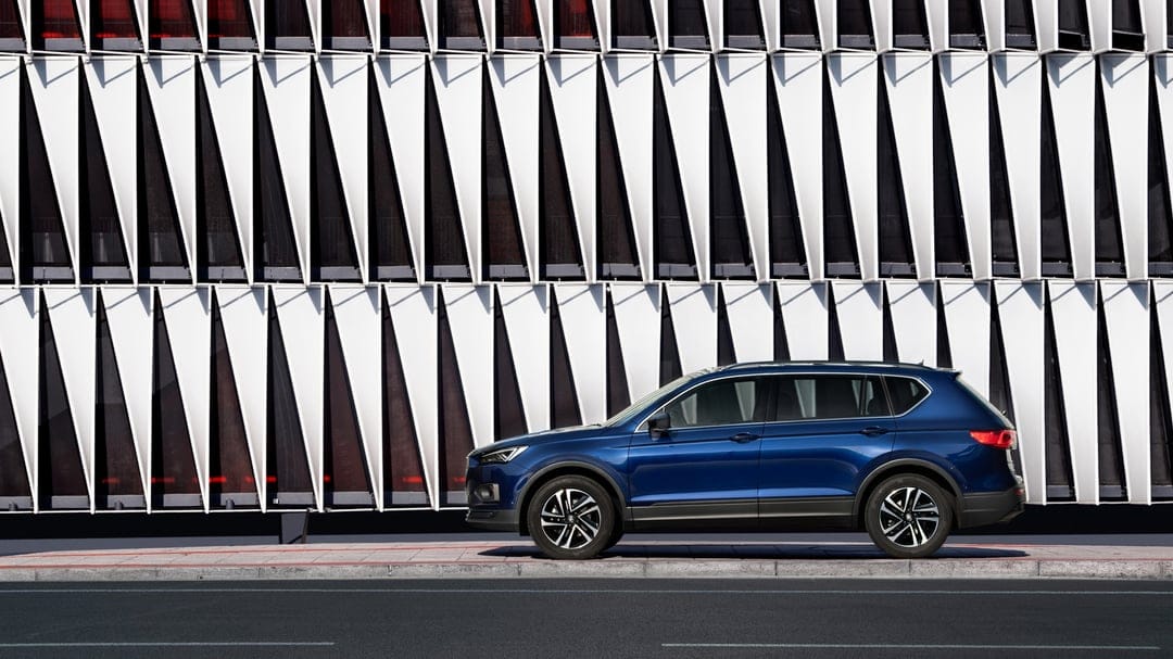 Blue SUV parked on an urban street in front of a modern building with white triangular geometric panels.