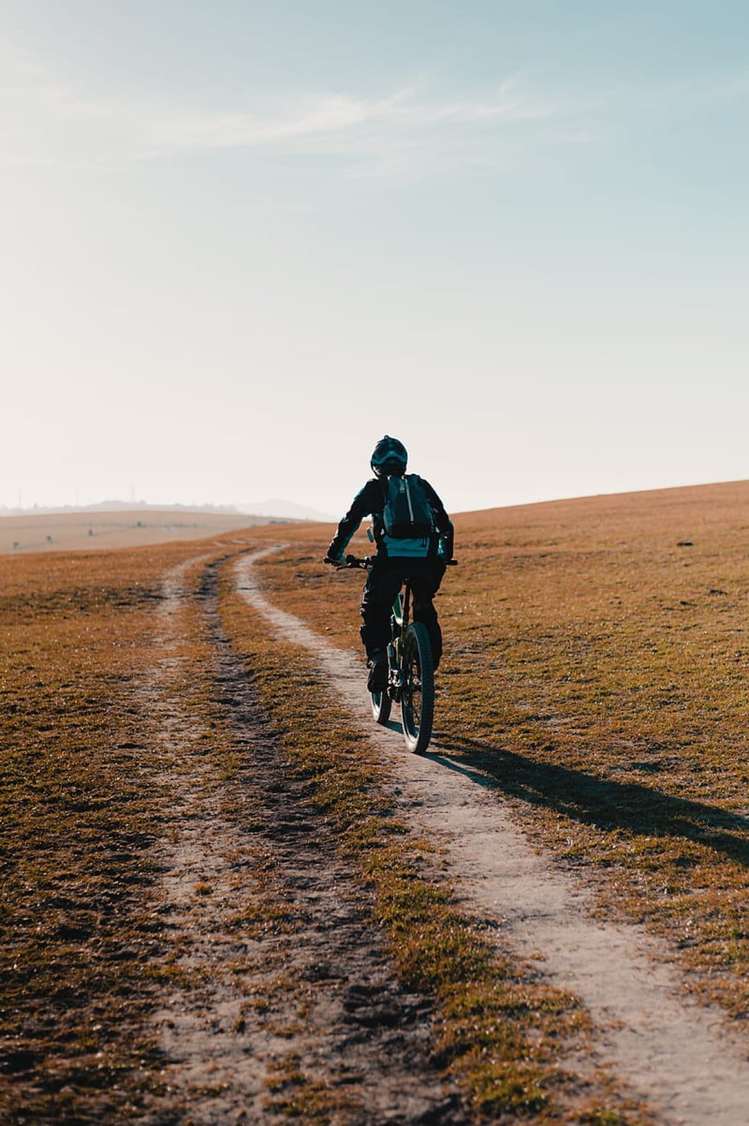 Mountain biker silhouetted against a bright sky while riding a dusty trail through a vast golden field.