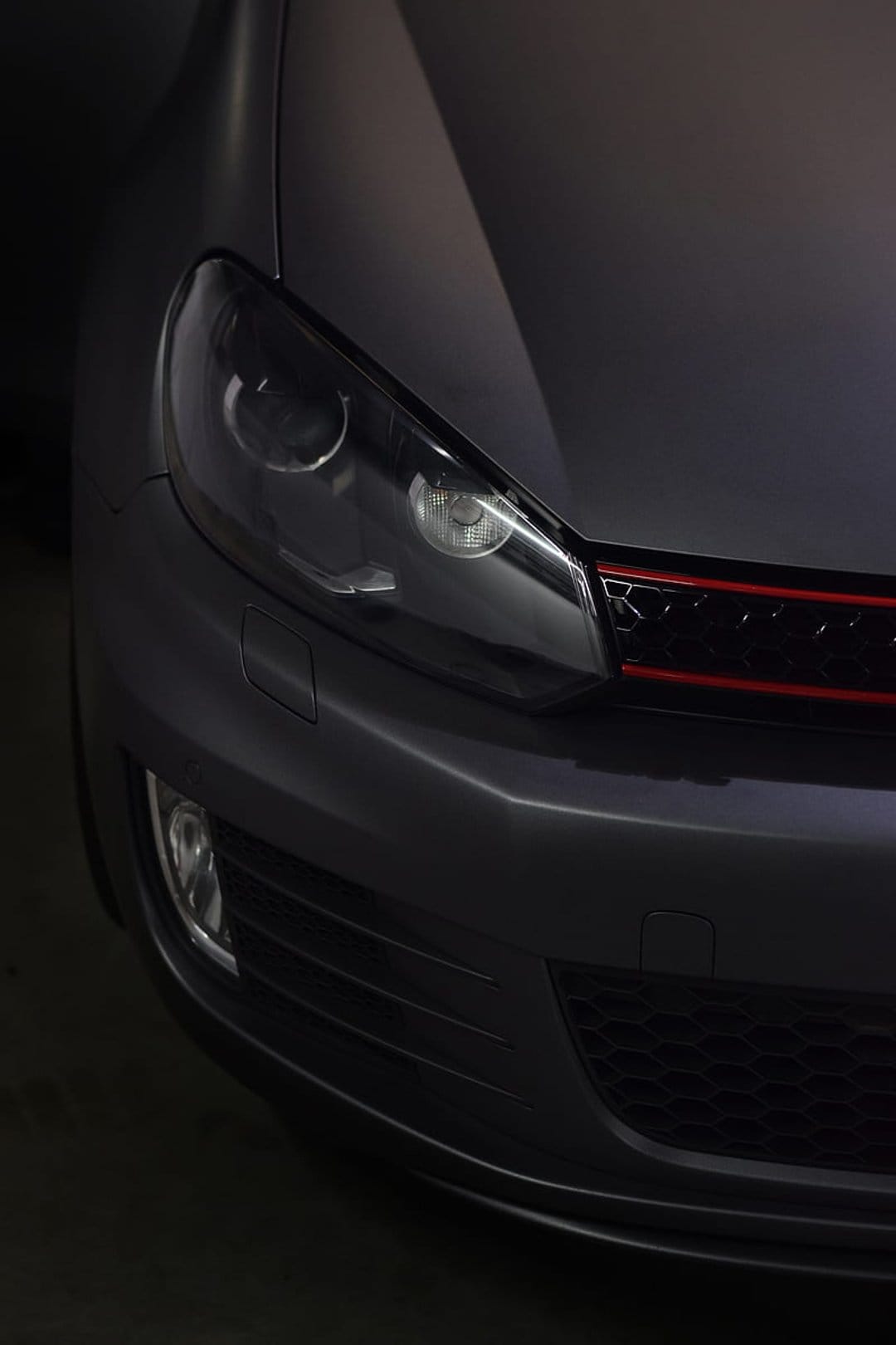 VW GTI front headlight and red accented honeycomb grille with a matte grey finish and dramatic low-angle lighting.