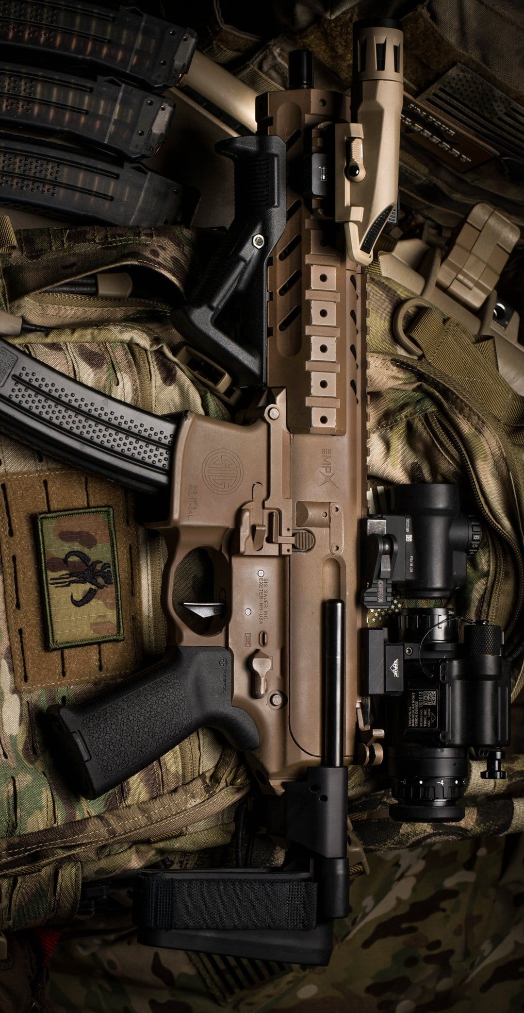Tan tactical AR pistol featuring advanced night vision optics and magazines on a textured military vest surface.