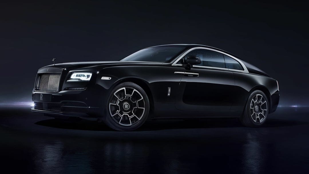 Side view of a black Rolls-Royce Wraith luxury car with chrome accents in a dark studio with dramatic lighting.