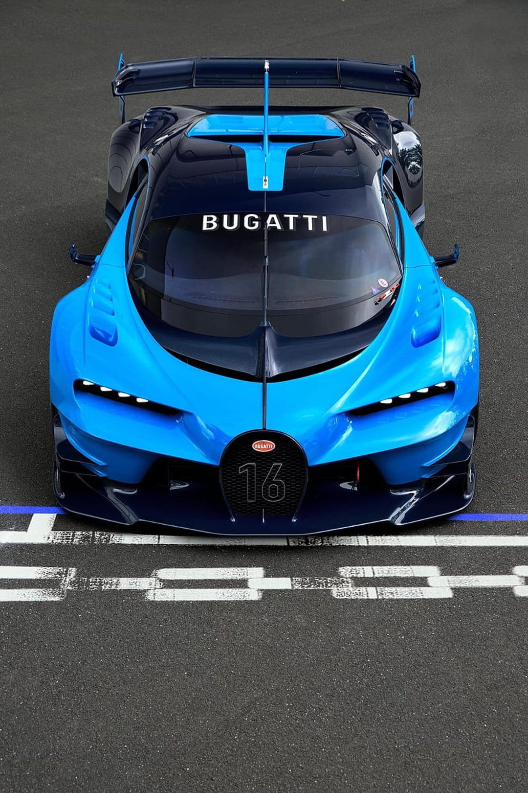 Bugatti Vision GT hypercar in blue and black racing across a dark asphalt track with white lines seen from above.