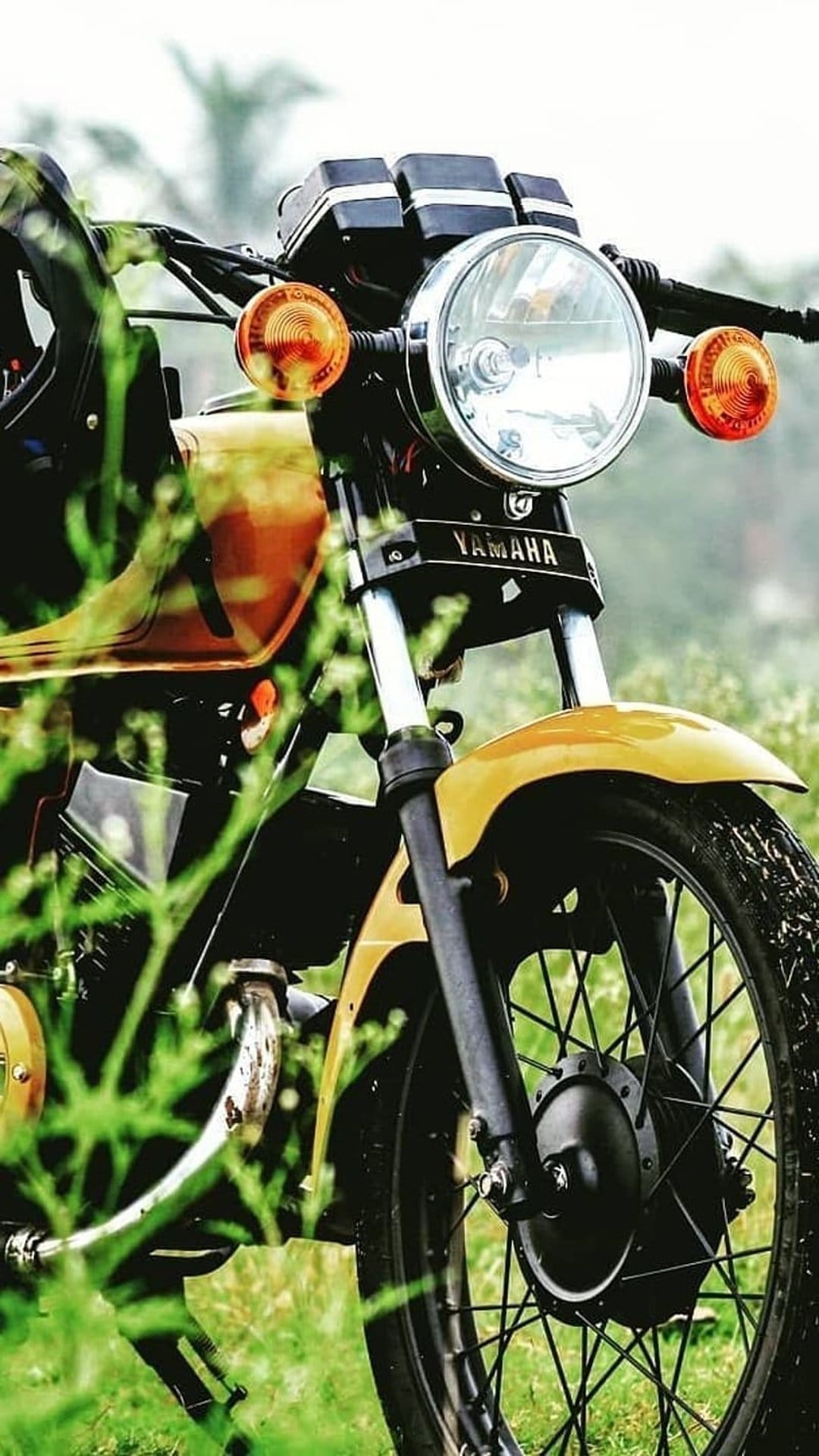 Yellow Yamaha motorcycle front featuring a round chrome headlight, orange blinkers, and a spoked off-road wheel.