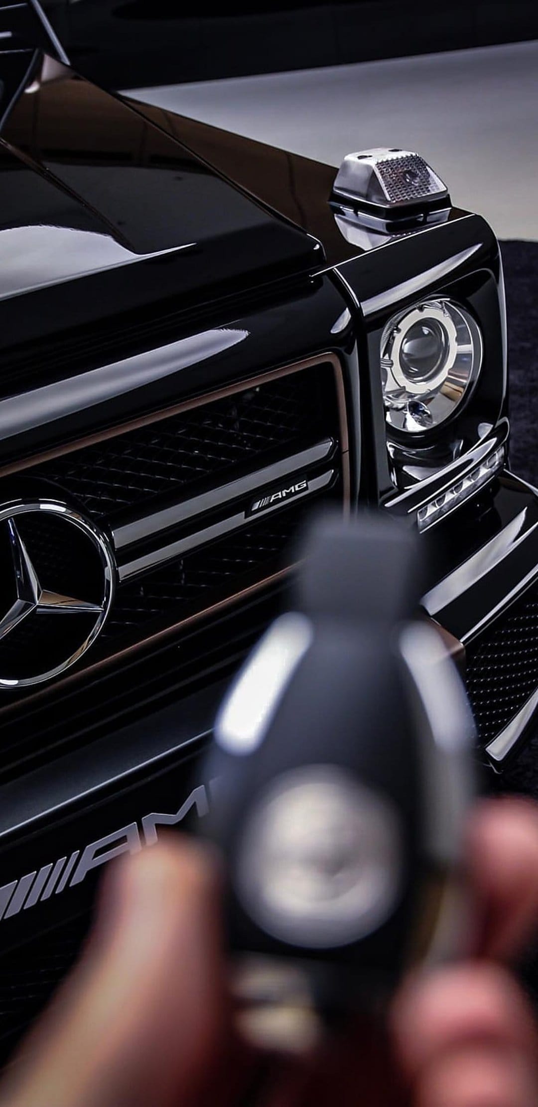 Mercedes G-Wagon front grille with chrome star emblem and a blurred car key held in the foreground.