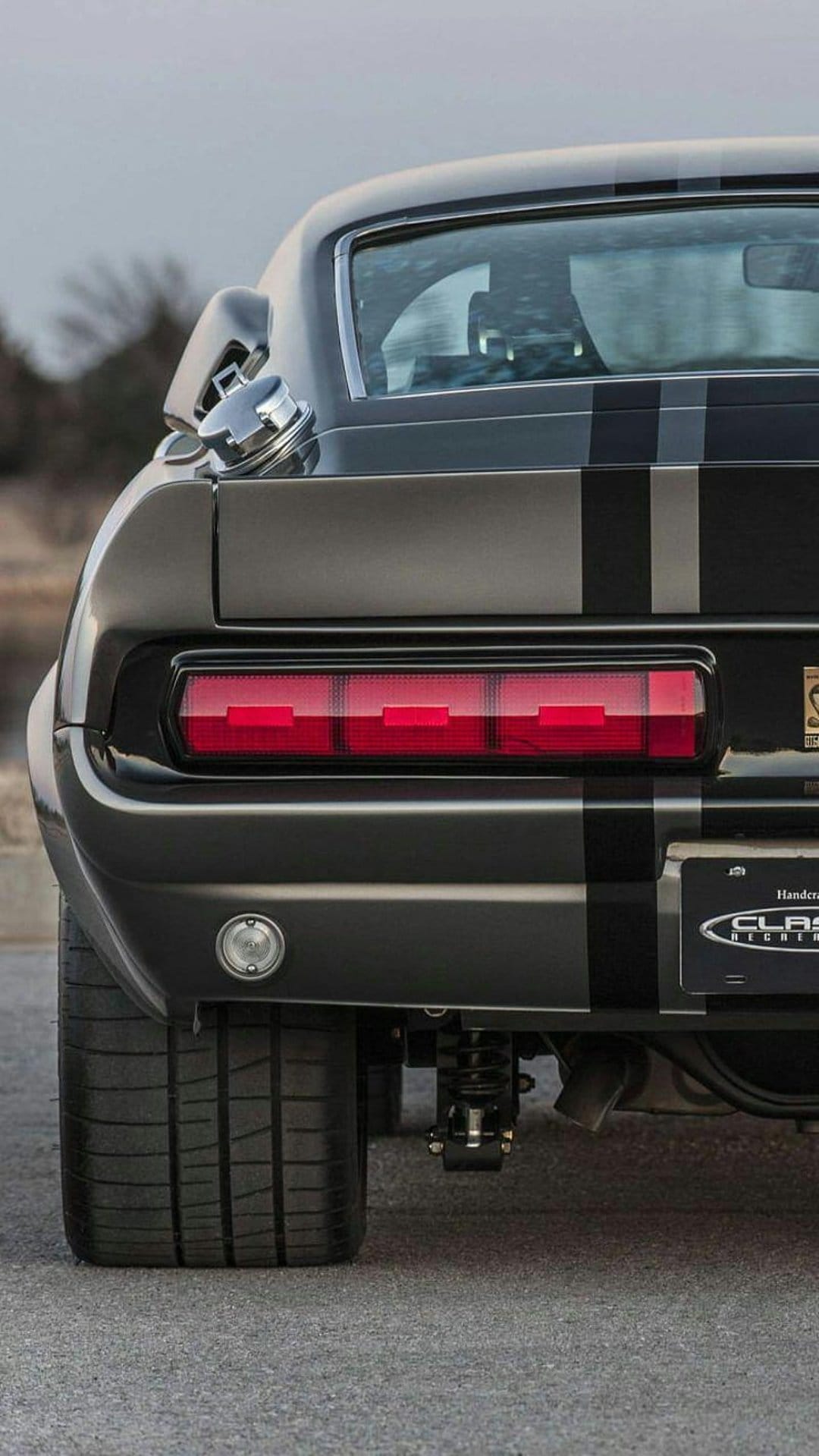 1967 Shelby GT500 rear with red tail lights, white racing stripes, and chrome gas cap on a vertical frame.