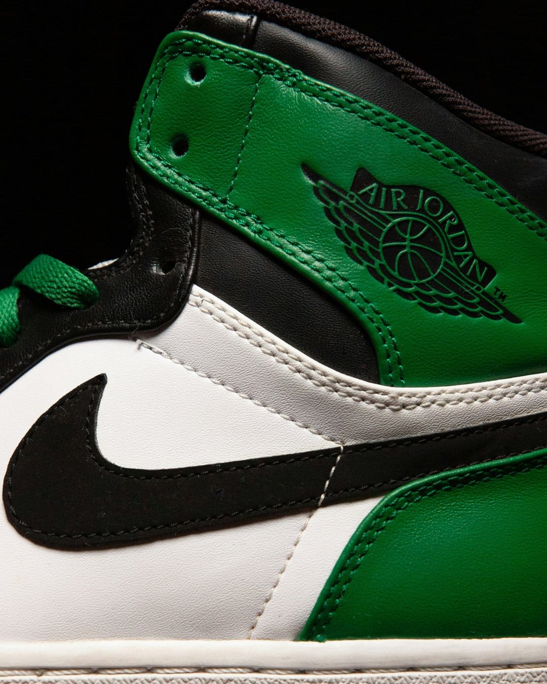 Air Jordan 1 Mid shoe with green leather accents, a black wings logo, and white panels shown in a close-up.