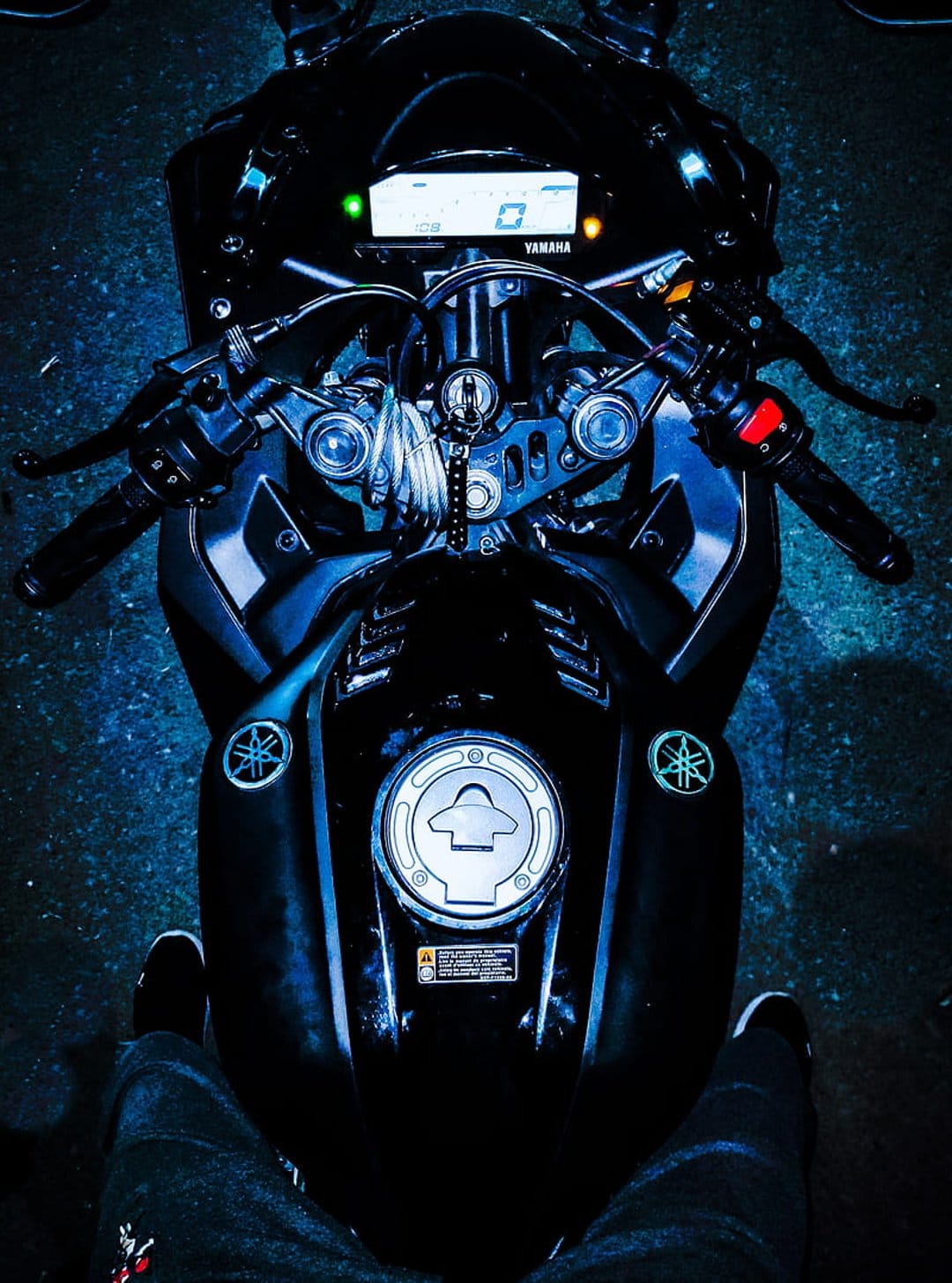 Yamaha R15 motorcycle cockpit showing the digital speedometer, handlebars, and fuel tank in dark blue tones.