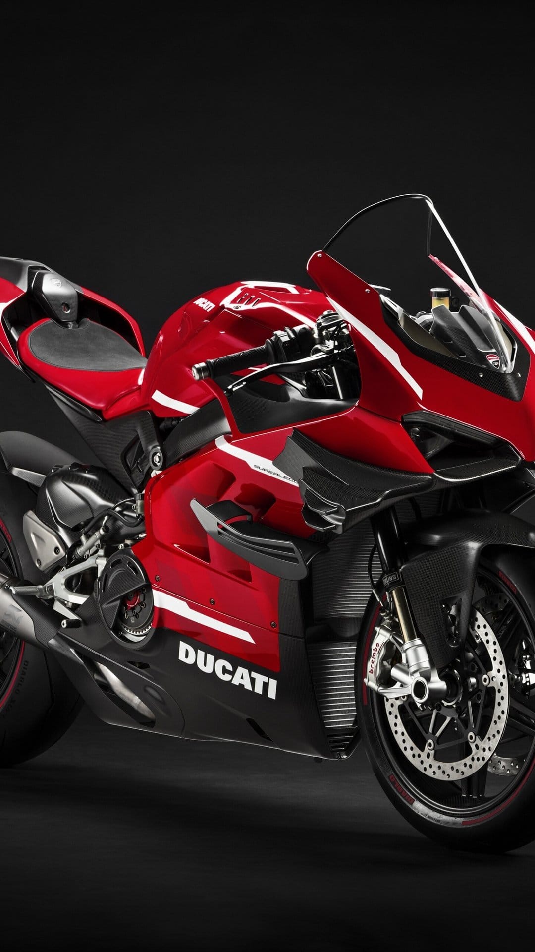 Close-up of a red Ducati Superleggera V4 motorcycle with carbon fiber winglets against a black background.
