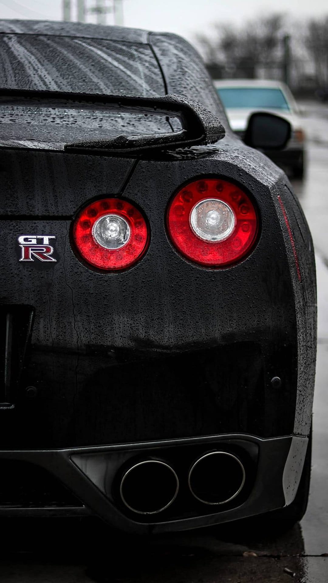Nissan GT-R circular red tail lights and silver badge on a wet black car body with raindrops and exhaust pipes.