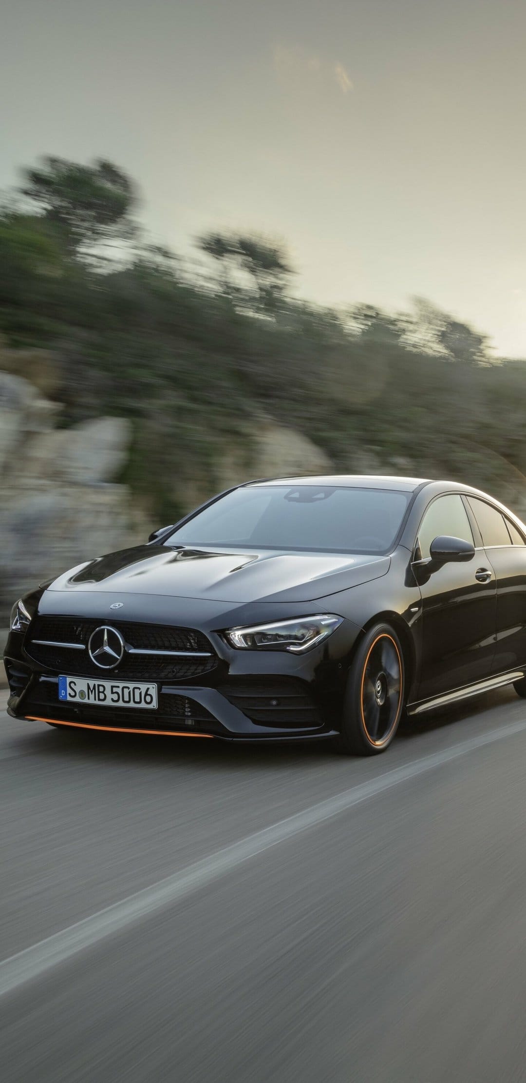Black Mercedes-Benz CLA luxury car driving on a road with motion blur and orange trim accents.
