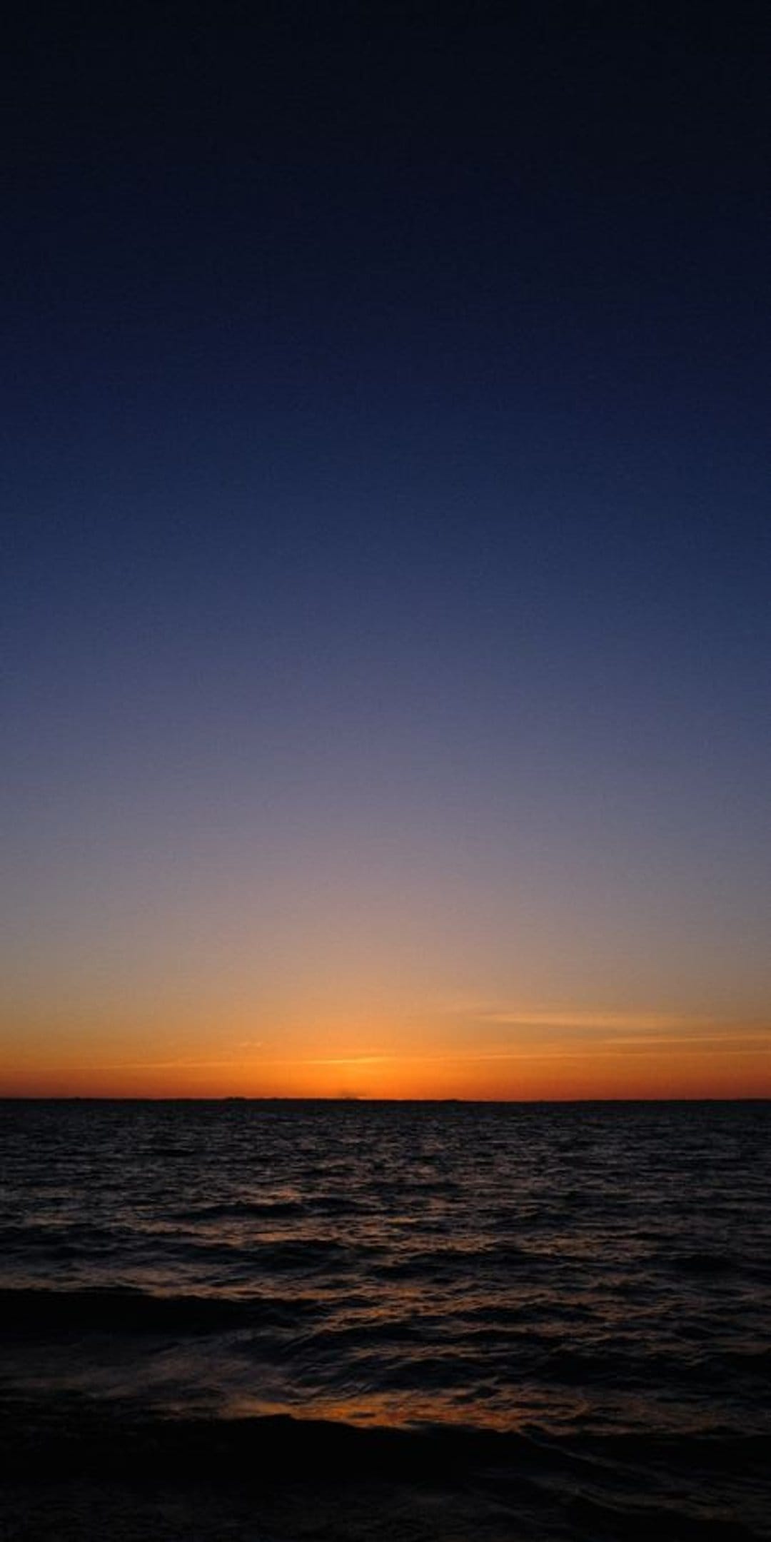 Dark ocean waves under a twilight sky fading from deep indigo to soft orange at the horizon line.