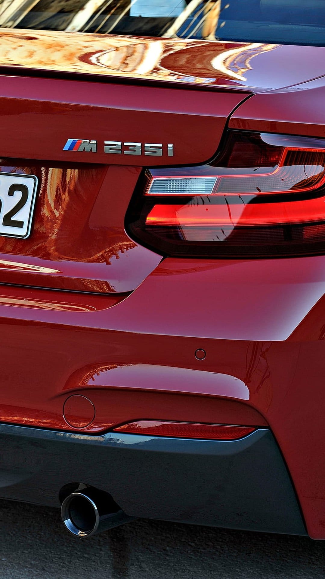 Red BMW M235i rear detail featuring a sharp LED tail light, M badge, and a polished metallic exhaust tip.