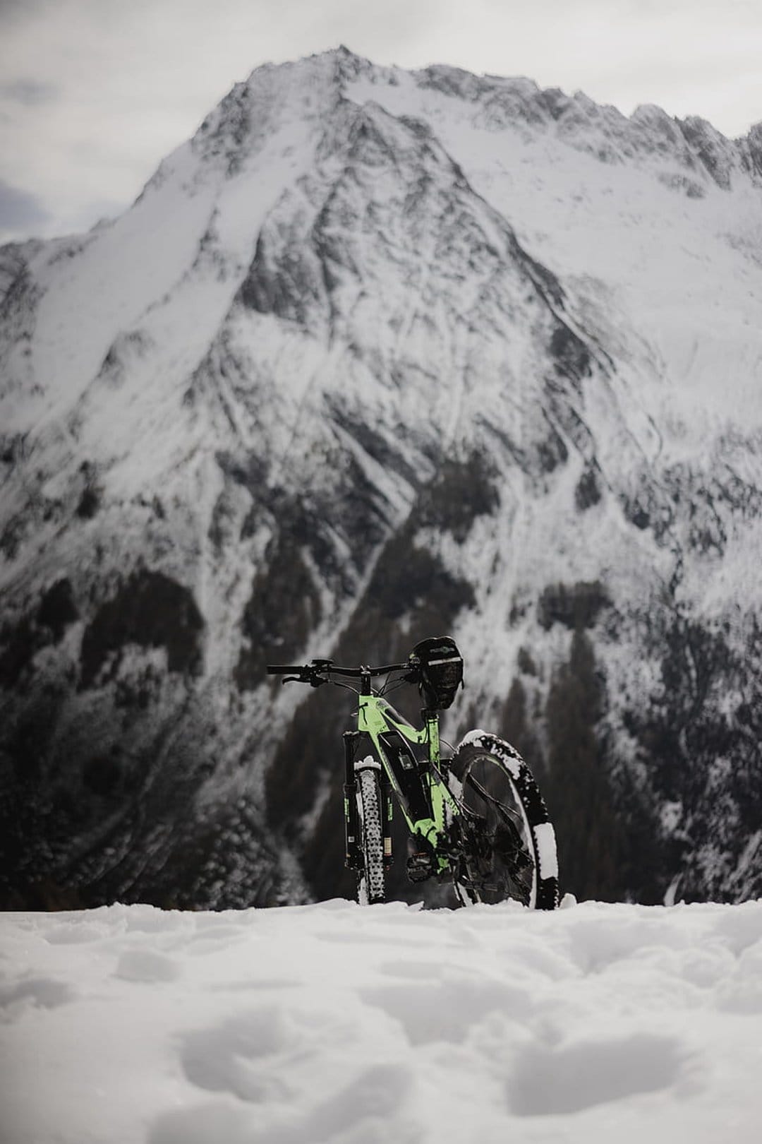 Neon green fat bike parked in deep white snow with massive jagged mountains under a clear winter sky.