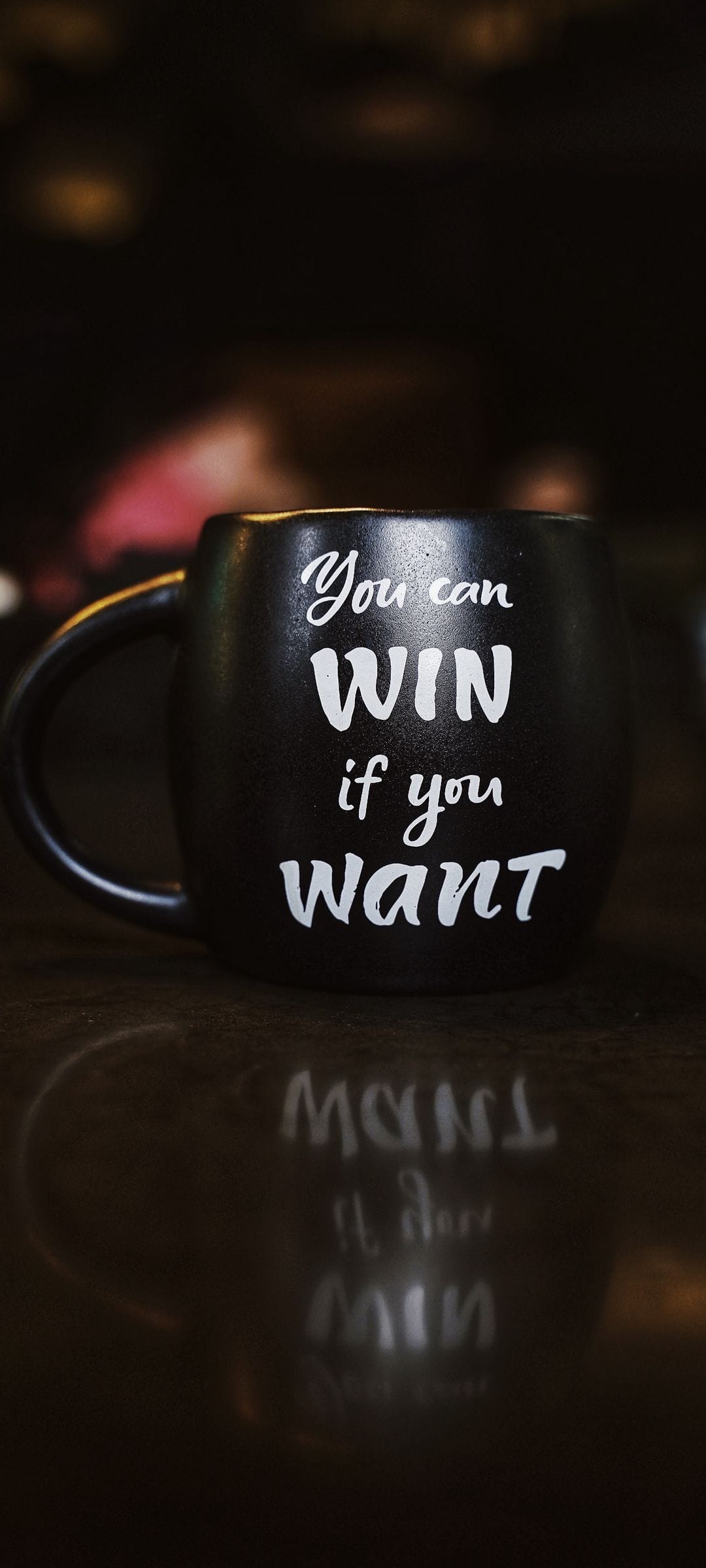 Black ceramic mug with You can WIN if you want text in white script on a dark reflective surface.