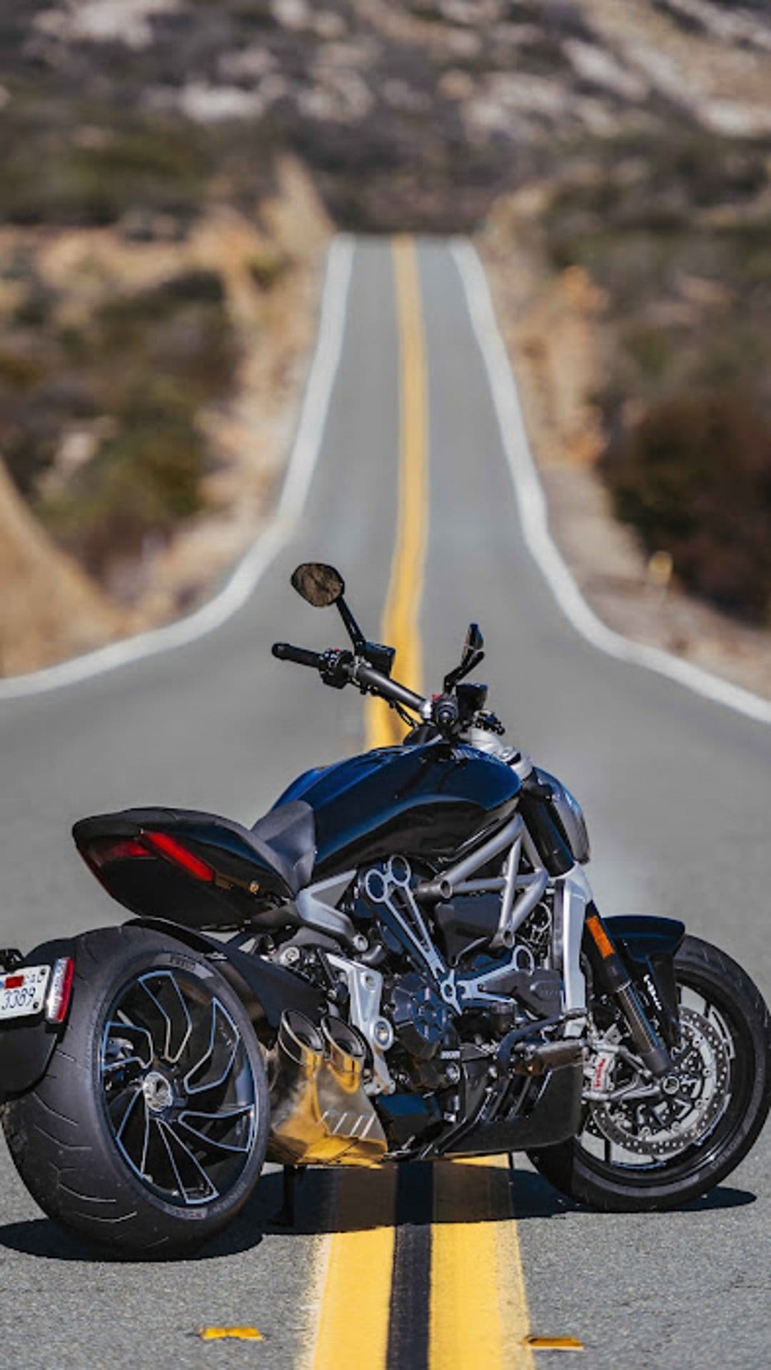 Black motorcycle parked on a winding asphalt road with double yellow lines leading toward hazy distant hills.
