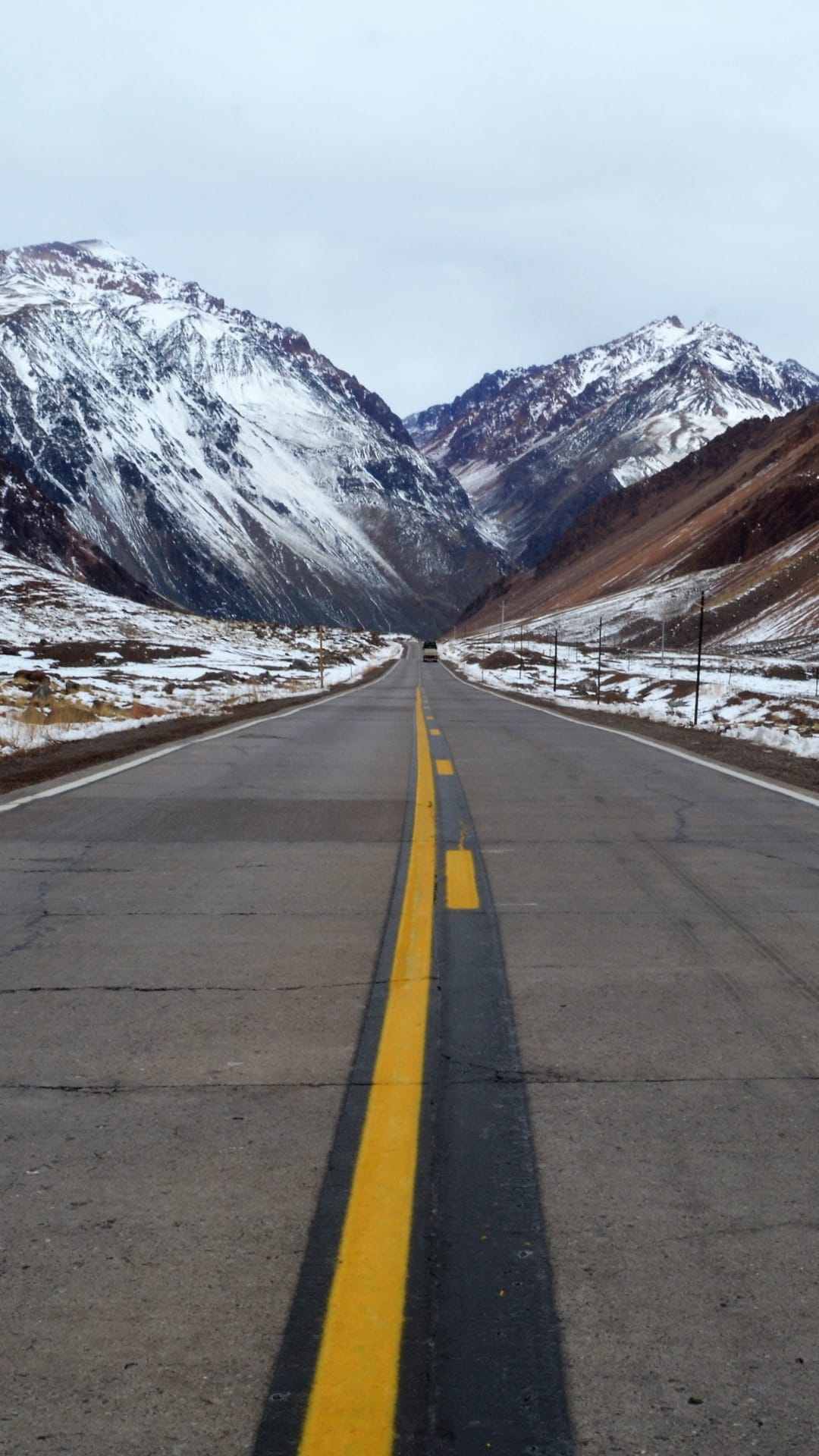 Straight asphalt road with a yellow center line stretches toward massive snow-covered mountain peaks in winter.