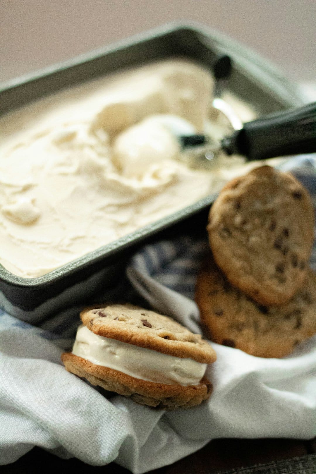 Chocolate chip cookie ice cream sandwich with melting vanilla center and visible chocolate chunks on a neutral plate.