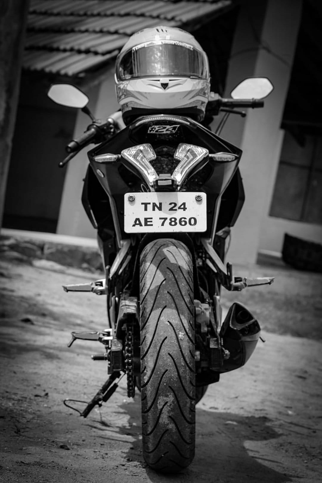 Motorcycle rear tire and taillights under a helmet on the handlebars in a black and white close-up shot.