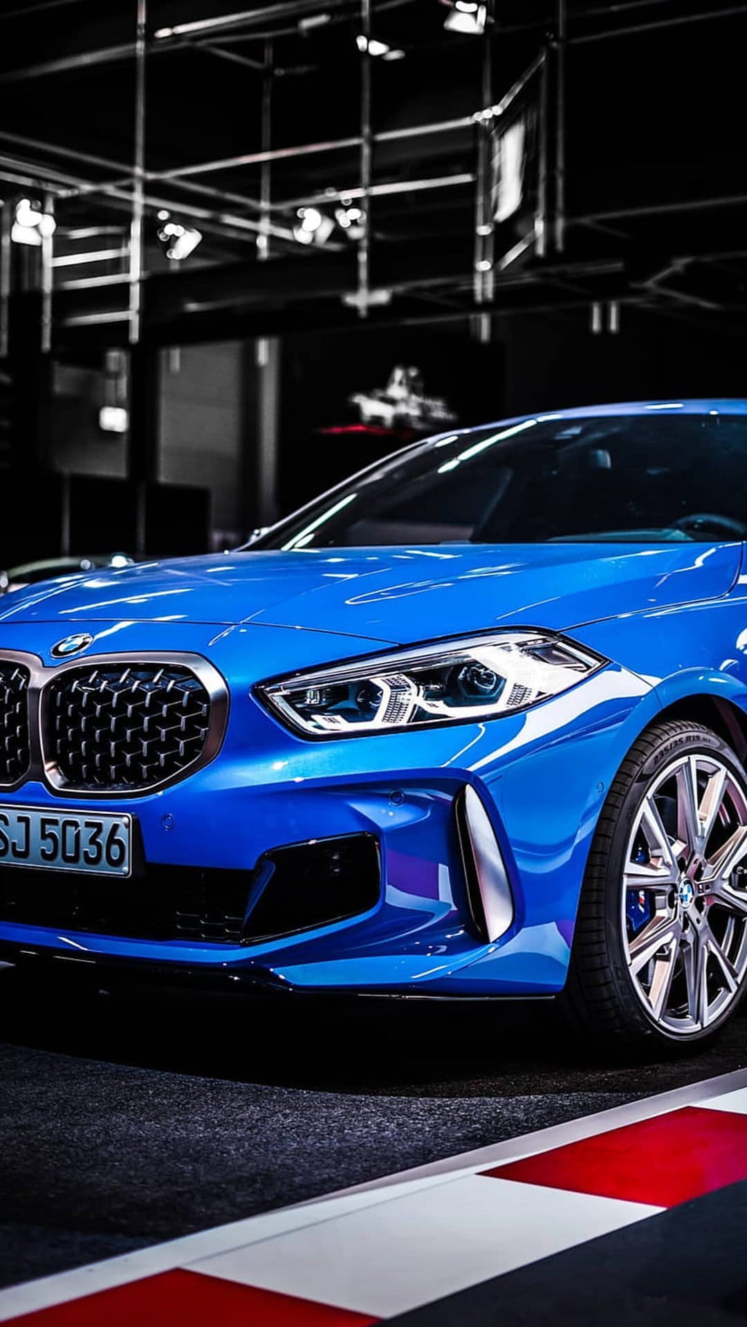 Blue BMW 1 Series hatchback featuring a black kidney grille and sharp LED headlights on a checkered floor.