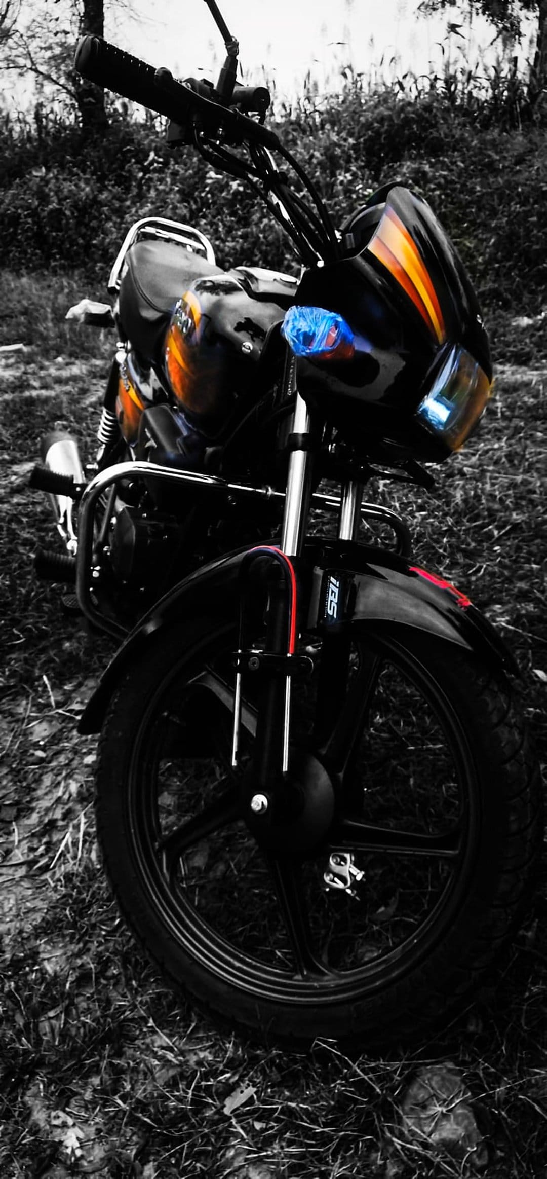 Black motorcycle front view with orange tank stripes and a glowing blue headlight against a blurred field.